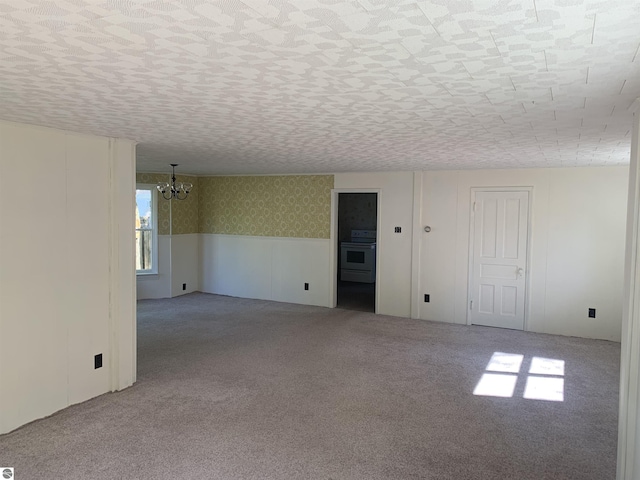 carpeted spare room with a chandelier, a wainscoted wall, and wallpapered walls