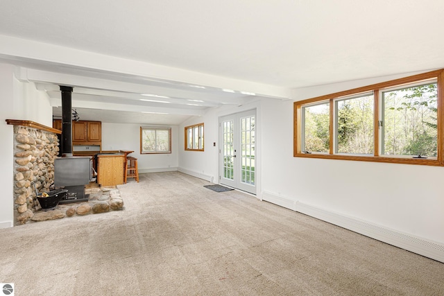11199 Center Rd, Traverse City, MI 49686 - unfurnished living room with a wood stove, light carpet, beam ceiling, a baseboard radiator, and baseboards