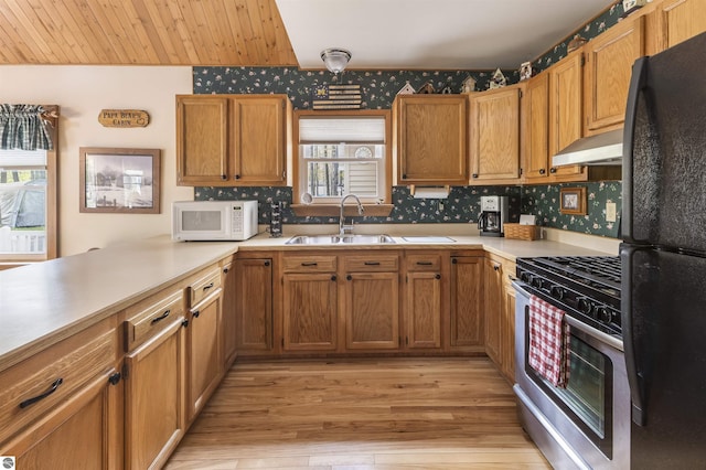 kitchen featuring white microwave, stainless steel gas range, a sink, under cabinet range hood, and freestanding refrigerator