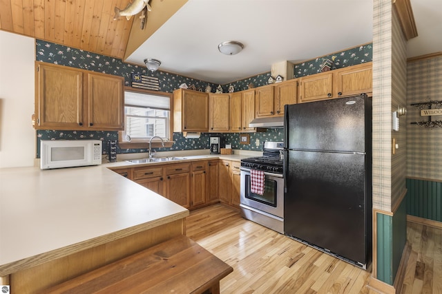 kitchen with freestanding refrigerator, wallpapered walls, stainless steel gas range, a sink, and white microwave