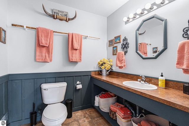 3290 Sumac Trl, Frankfort, MI 49635 - bathroom featuring stone finish flooring, toilet, a wainscoted wall, vanity, and a decorative wall