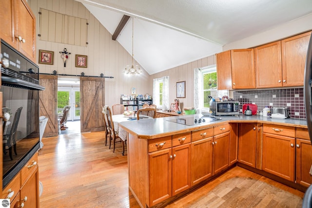 5817 Gross Dr, Weidman, MI 48893 - kitchen with light wood-style flooring, black appliances, a peninsula, brown cabinetry, and wood walls