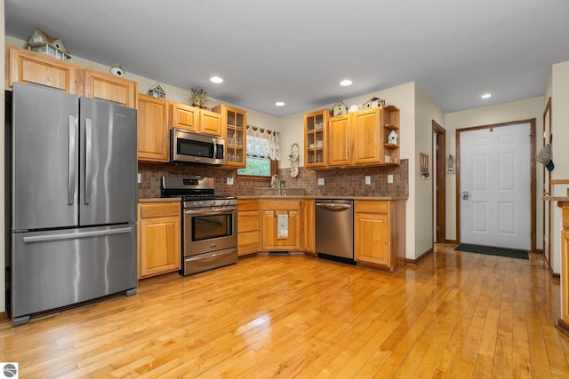 4611 Audubon Dr, Traverse City, MI 49686 - kitchen featuring stainless steel appliances, a sink, light wood finished floors, backsplash, and glass insert cabinets