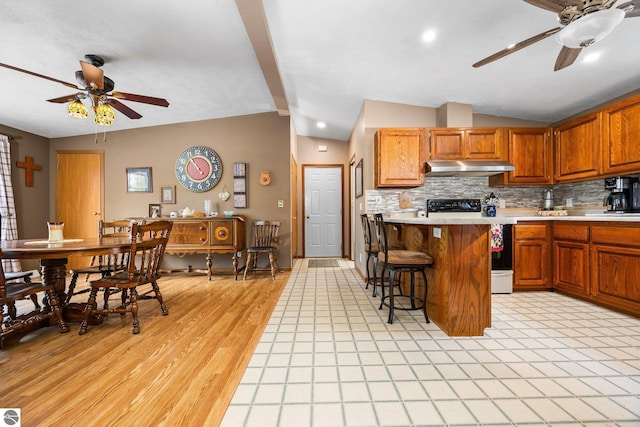 5206 S Riverview Dr, Lake City, MI 49651 - kitchen featuring ceiling fan, under cabinet range hood, range with electric stovetop, a breakfast bar area, and decorative backsplash