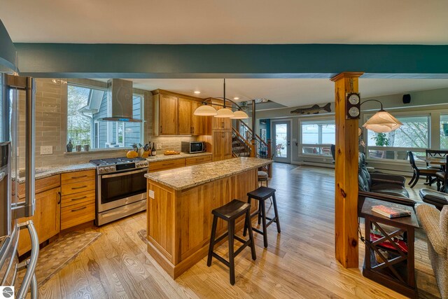 6433 S W Bayshore Dr, Traverse City, MI 49684 - kitchen featuring appliances with stainless steel finishes, light wood-style flooring, wall chimney range hood, a center island, and backsplash