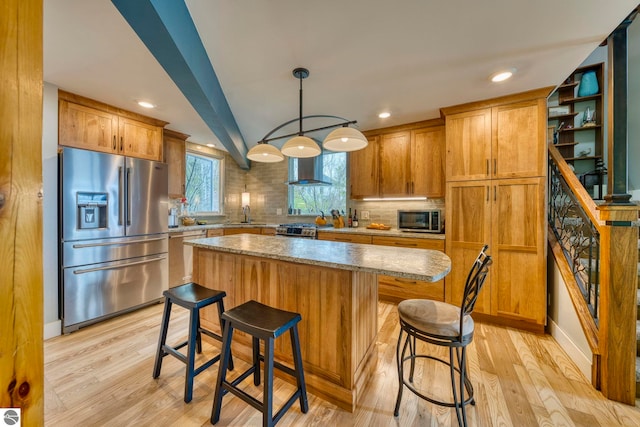 6433 S W Bayshore Dr, Traverse City, MI 49684 - kitchen featuring appliances with stainless steel finishes, wall chimney exhaust hood, light wood-type flooring, tasteful backsplash, and a center island