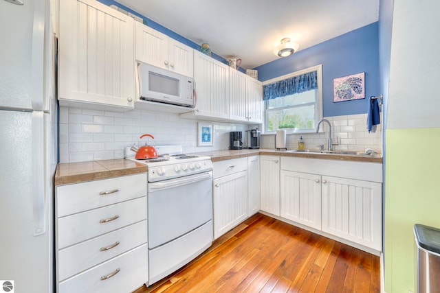 6433 S W Bayshore Dr, Traverse City, MI 49684 - kitchen featuring white appliances, light wood-type flooring, tasteful backsplash, a sink, and white cabinets