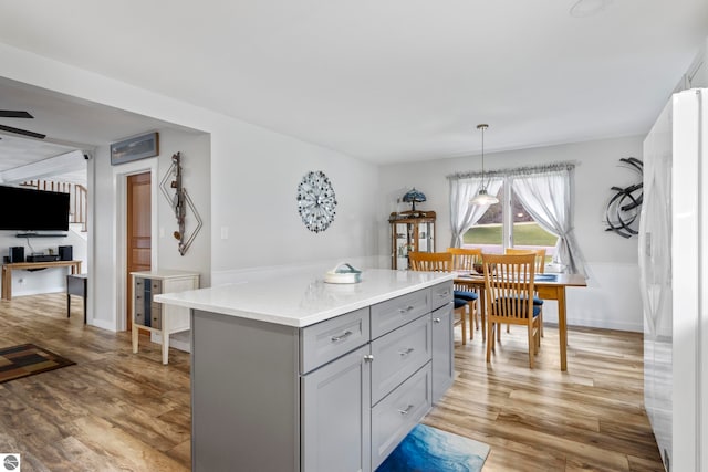 7256 Highland Dr, Beulah, MI 49617 - kitchen featuring gray cabinetry, freestanding refrigerator, light wood finished floors, a center island, and hanging light fixtures
