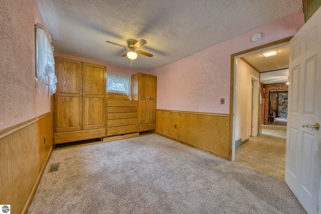 4253 S Garfield Rd, Kingsley, MI 49649 - unfurnished bedroom featuring wood walls, a textured ceiling, wainscoting, a textured wall, and light colored carpet