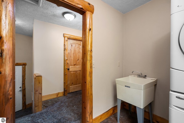 5592 Troon N, Bellaire, MI 49615 - washroom featuring a textured ceiling, baseboards, stacked washing machine and dryer, and a sink