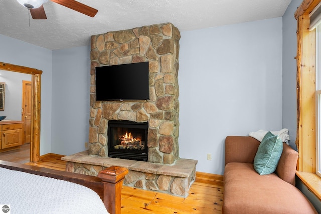 5592 Troon N, Bellaire, MI 49615 - bedroom with wood finished floors, a fireplace, a textured ceiling, baseboards, and ceiling fan