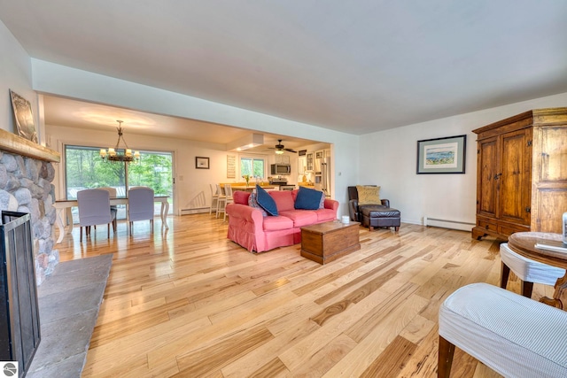 310 W Broadway, Suttons Bay, MI 49682 - living room with a baseboard radiator, light wood-type flooring, a stone fireplace, a chandelier, and a ceiling fan