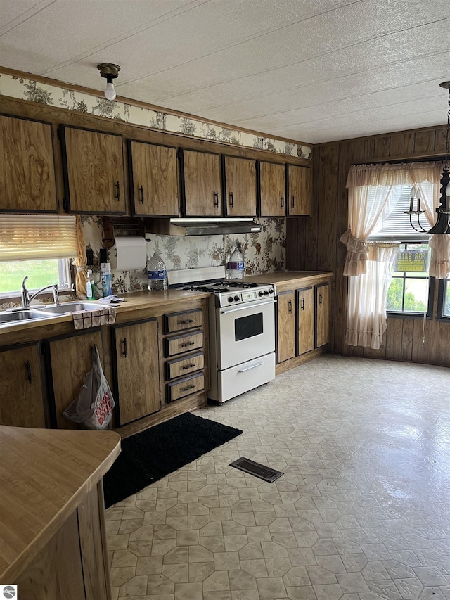 118 W Huron, Omer, MI 48749 - kitchen featuring white gas stove, a sink, plenty of natural light, wooden walls, and under cabinet range hood