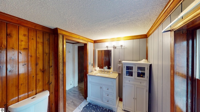 605 Cedar Ave, Houghton Lake, MI 48651 - bathroom featuring vanity, wood finished floors, toilet, a textured ceiling, and wooden walls