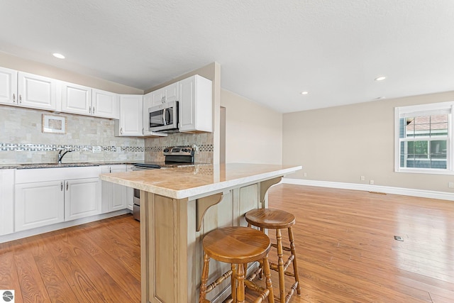 3151 W Lake Mitchell Dr, Cadillac, MI 49601 - kitchen with appliances with stainless steel finishes, a breakfast bar area, a sink, light wood-style floors, and recessed lighting