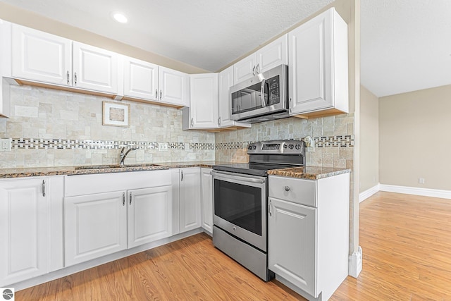 3151 W Lake Mitchell Dr, Cadillac, MI 49601 - kitchen featuring appliances with stainless steel finishes, stone countertops, light wood-style floors, white cabinets, and baseboards