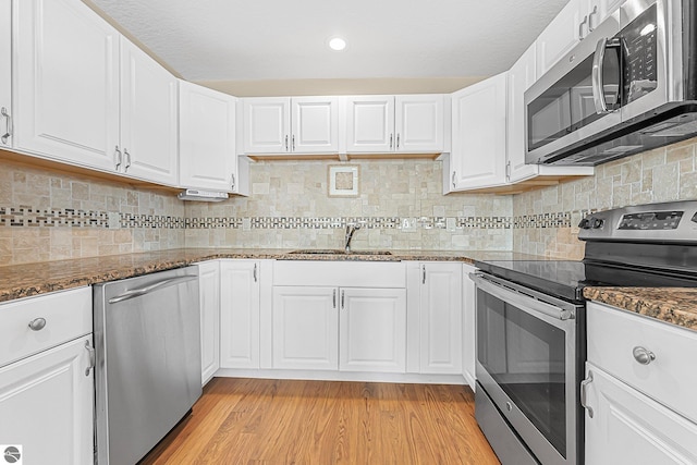 3151 W Lake Mitchell Dr, Cadillac, MI 49601 - kitchen with appliances with stainless steel finishes, a sink, white cabinetry, light wood-type flooring, and dark stone countertops