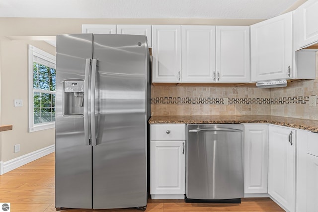 3151 W Lake Mitchell Dr, Cadillac, MI 49601 - kitchen featuring stainless steel appliances, white cabinetry, dark stone counters, decorative backsplash, and light wood-type flooring