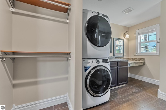 3151 W Lake Mitchell Dr, Cadillac, MI 49601 - washroom with stacked washer / dryer, baseboards, dark wood-style flooring, and cabinet space