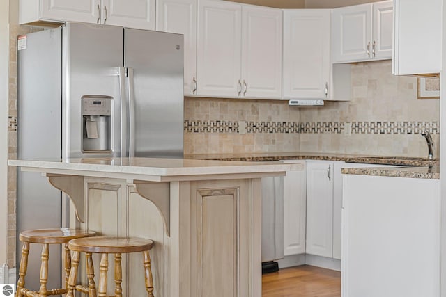 3151 W Lake Mitchell Dr, Cadillac, MI 49601 - kitchen featuring a sink, tasteful backsplash, white cabinetry, a breakfast bar, and light wood-style floors