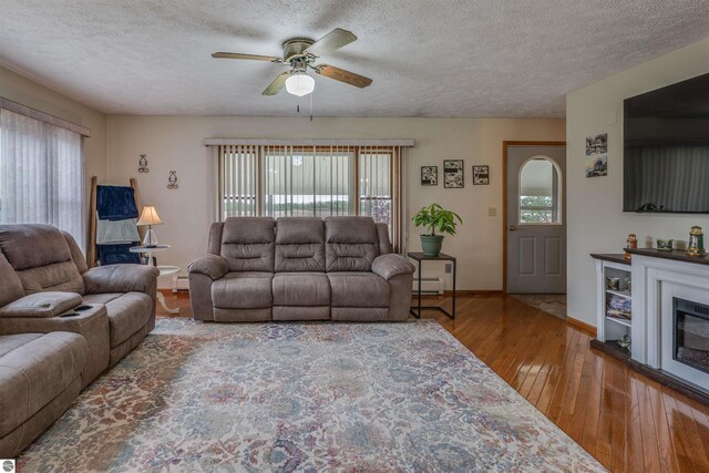 605 E M-55, West Branch, MI 48661 - living room featuring hardwood / wood-style floors, a ceiling fan, a textured ceiling, baseboards, and baseboard heating