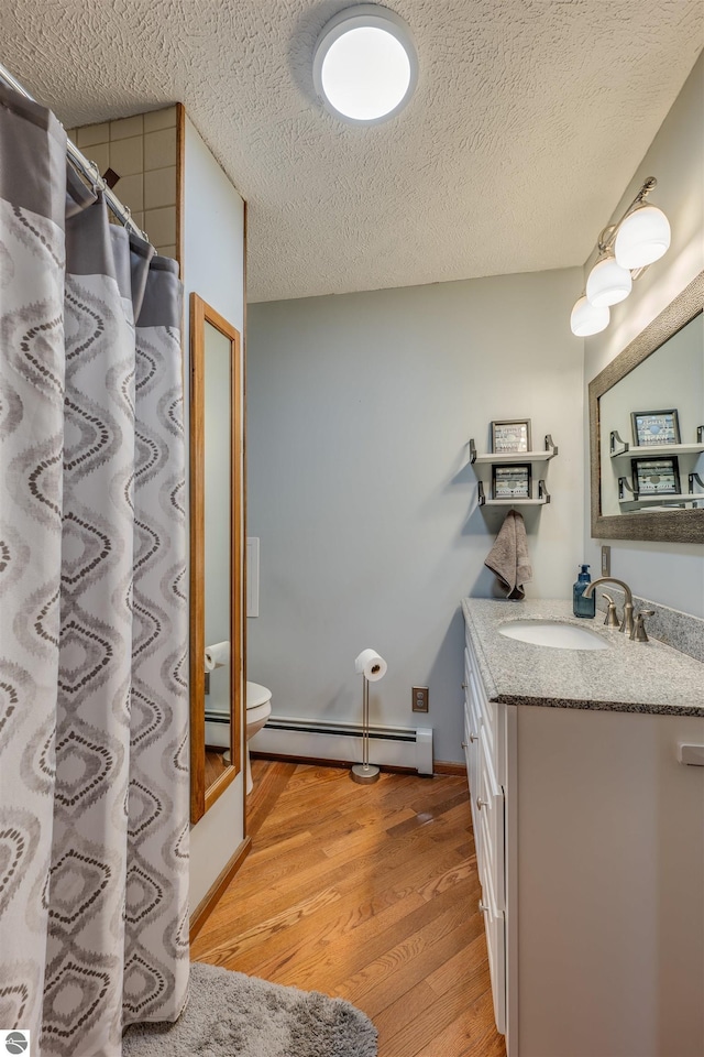 605 E M-55, West Branch, MI 48661 - bathroom featuring vanity, wood finished floors, a baseboard heating unit, toilet, and a textured ceiling