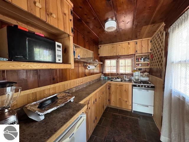 951 Lake Dr, Harrison, MI 48625 - kitchen with white gas stove, wood ceiling, black microwave, wooden walls, and dark countertops