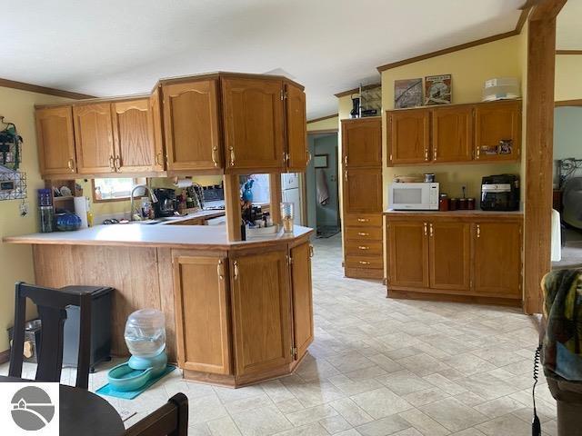 10559 Rosted Rd, Lake City, MI 49651 - kitchen with brown cabinets, white microwave, crown molding, light countertops, and lofted ceiling