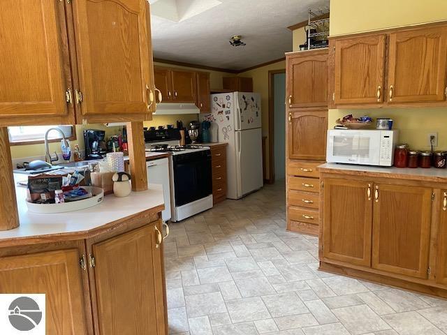 10559 Rosted Rd, Lake City, MI 49651 - kitchen with white appliances, ventilation hood, light countertops, brown cabinets, and crown molding