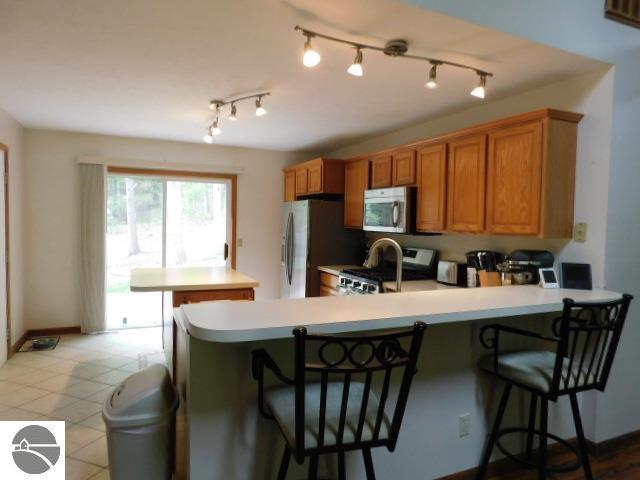 12149 Cabin Ln, Rapid City, MI 49676 - kitchen featuring appliances with stainless steel finishes, a peninsula, light countertops, and brown cabinetry