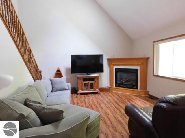 12149 Cabin Ln, Rapid City, MI 49676 - living room with wood finished floors, vaulted ceiling, a glass covered fireplace, stairs, and baseboards