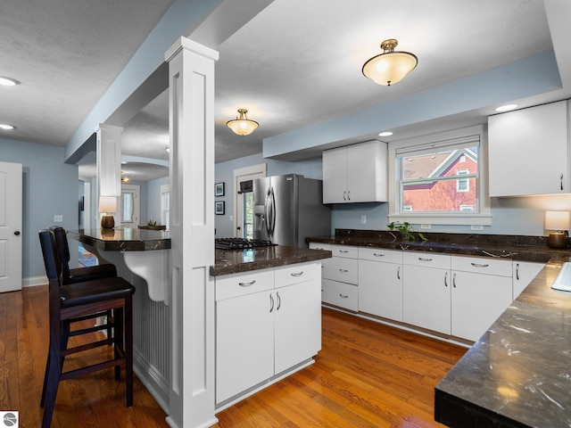 855 E State St, Traverse City, MI 49686 - kitchen featuring stainless steel fridge, decorative columns, gas cooktop, white cabinets, and hardwood / wood-style floors