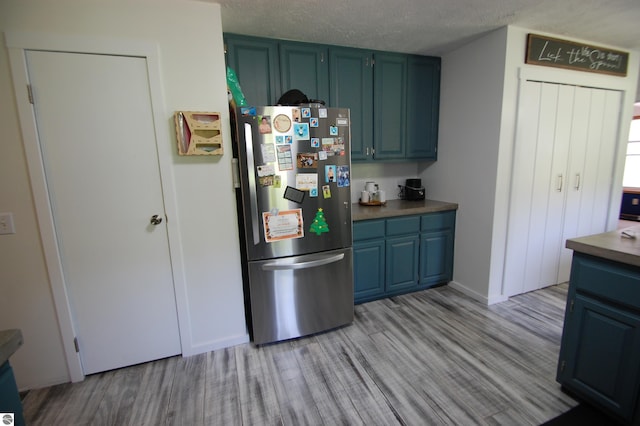 1137 Stoney Ridge Rd, West Branch, MI 48661 - kitchen with freestanding refrigerator, light wood-type flooring, blue cabinetry, and a textured ceiling