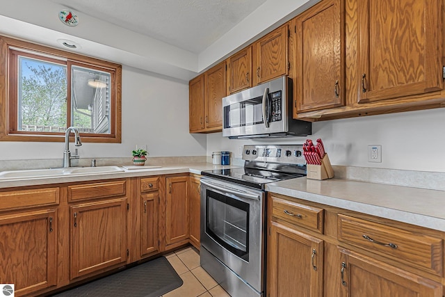 2683 Green Meadows Dr Unit 10, Traverse City, MI 49685 - kitchen featuring stainless steel appliances, a sink, brown cabinetry, light tile patterned floors, and light countertops
