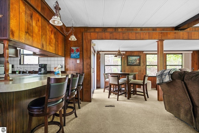 1912 Rosenburg Rd, Kalkaska, MI 49646 - kitchen with light carpet, wood walls, a kitchen breakfast bar, pendant lighting, and brown cabinets
