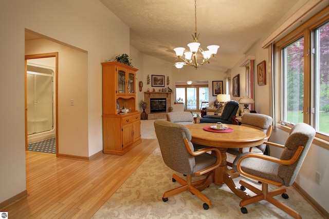 1162 Hemingway Ln, Traverse City, MI 49686 - dining room with light wood-type flooring, a chandelier, a tiled fireplace, baseboards, and vaulted ceiling