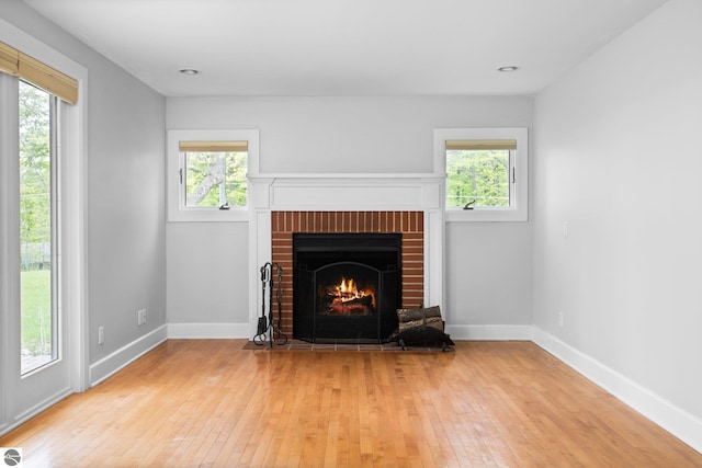 6675 Walker St, Benzonia, MI 49616 - unfurnished living room featuring wood-type flooring, healthy amount of natural light, a brick fireplace, and baseboards