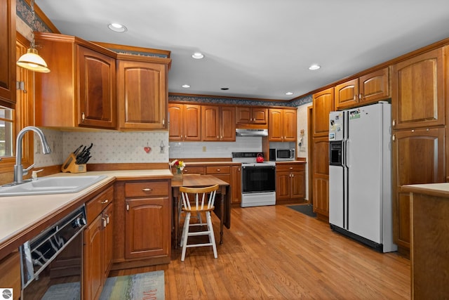 906 Michigan Ave, Frankfort, MI 49635 - kitchen featuring white appliances, a sink, under cabinet range hood, brown cabinetry, and light wood-style floors