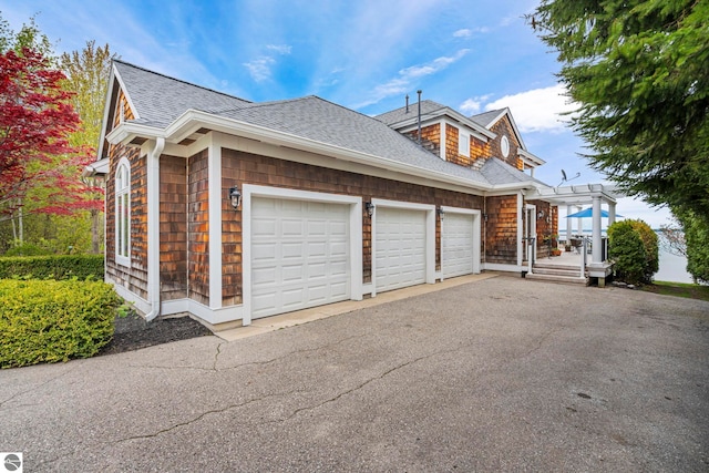 6853 S W Bay Shore Dr, Traverse City, MI 49684 - view of side of home with roof with shingles, driveway, an attached garage, and a pergola