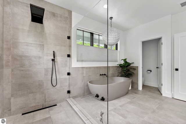 6848 S Carol Ann Dr, Traverse City, MI 49684 - full bath featuring a freestanding bath, walk in shower, tile walls, and toilet