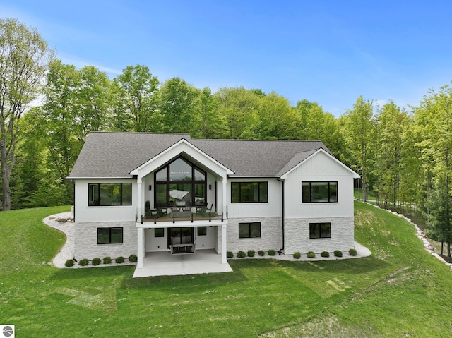 6848 S Carol Ann Dr, Traverse City, MI 49684 - rear view of house featuring a patio, stone siding, a lawn, and a shingled roof