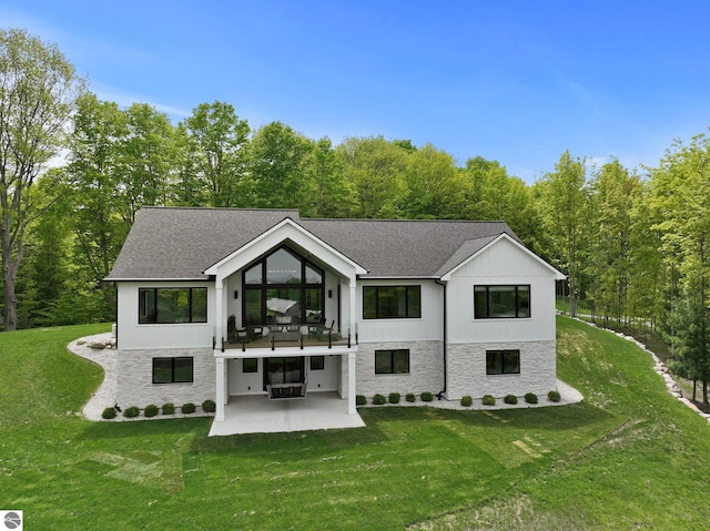 6848 S Carol Ann Dr, Traverse City, MI 49684 - rear view of property with a patio area, stone siding, a lawn, and roof with shingles