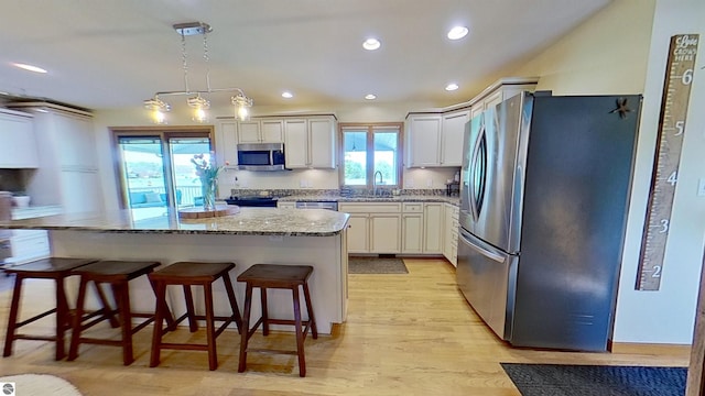 2152 Cornerstone Dr, Mount Pleasant, MI 48858 - kitchen featuring appliances with stainless steel finishes, a sink, light stone countertops, a breakfast bar area, and light wood finished floors