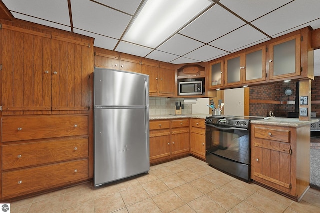 217 Winona Pl, Cadillac, MI 49601 - kitchen with appliances with stainless steel finishes, brown cabinets, light tile patterned flooring, a drop ceiling, and glass insert cabinets