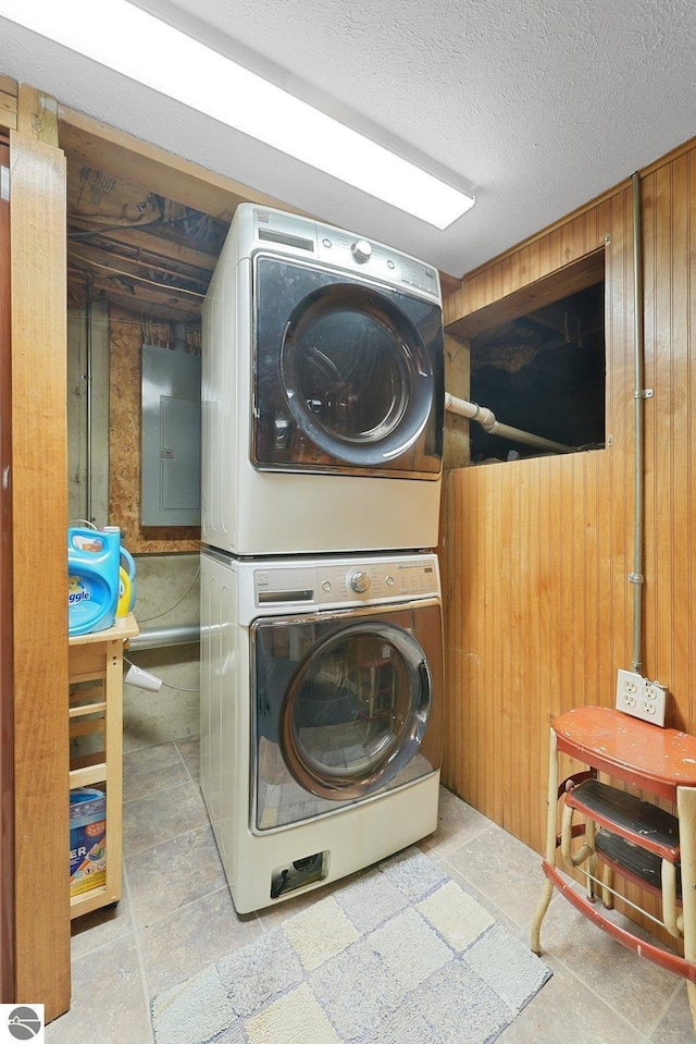 217 Winona Pl, Cadillac, MI 49601 - laundry room featuring stacked washer and clothes dryer, electric panel, stone tile floors, wood walls, and a textured ceiling