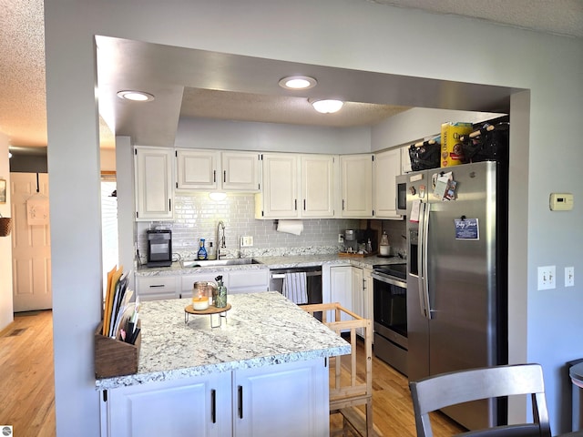 902 S Crapo St, Mount Pleasant, MI 48858 - kitchen featuring a sink, stainless steel appliances, white cabinets, backsplash, and light wood-style flooring