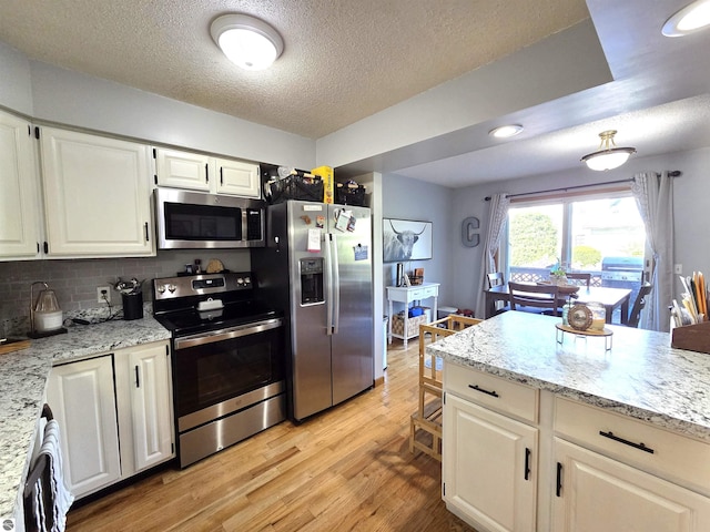 902 S Crapo St, Mount Pleasant, MI 48858 - kitchen with appliances with stainless steel finishes, light wood-style flooring, white cabinets, a textured ceiling, and decorative backsplash