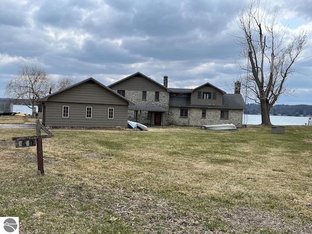 3171 Midway Dr, Onekama, MI 49675 - back of house with a chimney, stone siding, and a yard