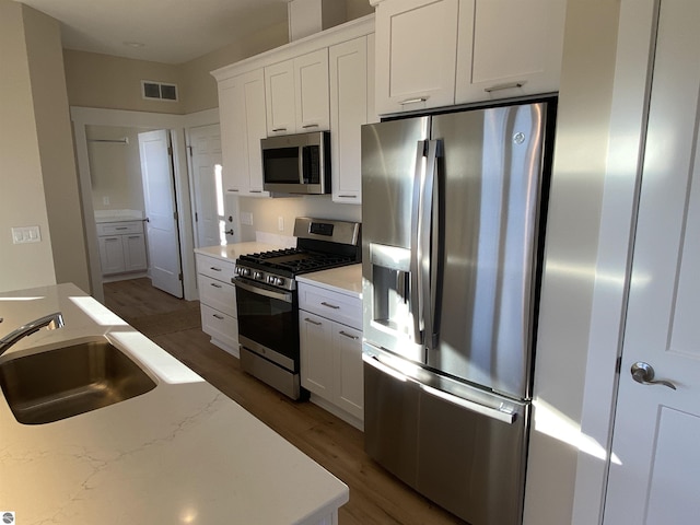 7559 E Meadows Dr Unit 52, Traverse City, MI 49621 - kitchen featuring stainless steel appliances, a sink, wood finished floors, white cabinets, and light stone countertops