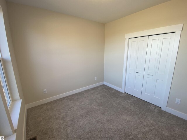 7559 E Meadows Dr Unit 52, Traverse City, MI 49621 - unfurnished bedroom with dark carpet, baseboards, and a closet